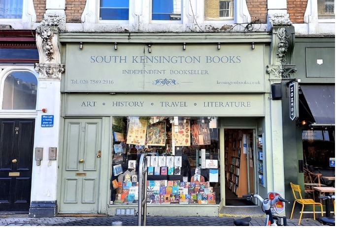Photo of the front of a bookshop. The front is light green and books are visible in the window. The name of the shop is South Kensington Books. https://www.kensingtonbooks.co.uk/